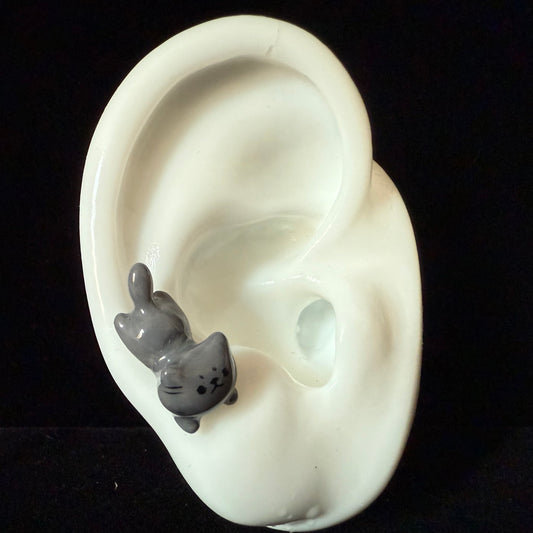 Gray cat-shaped earring on a white ear model against a black background
