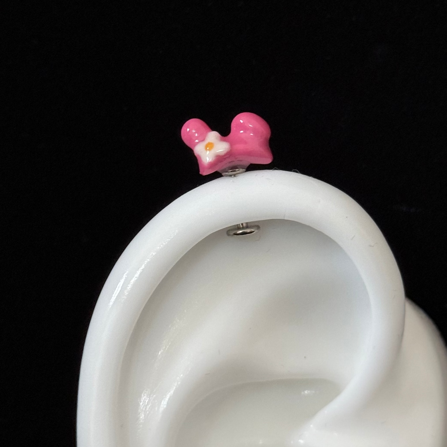 Pink bow-shaped earring on a white ear model against a black background